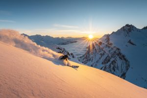 A skier carves down a powder slope in Zürs during golden sunset light above a sea of clouds