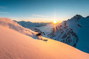 A skier carves down a powder slope in Zürs during golden sunset light above a sea of clouds